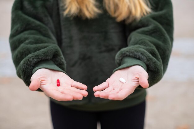 Seção média de mulher com pílula vermelha e branca de pé na estrada