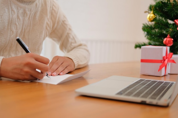 Foto seção média de mulher fazendo cartão de saudação enquanto está sentada na mesa em casa durante o natal