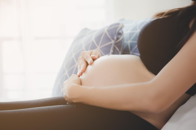 Seção média de mulher grávida com as mãos na barriga sentada no sofá