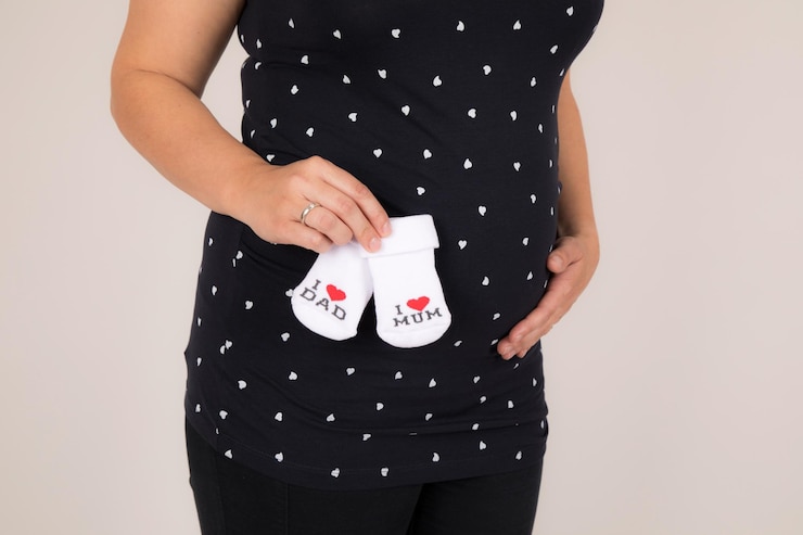 Foto seção média de mulher grávida segurando meias de bebê contra fundo branco