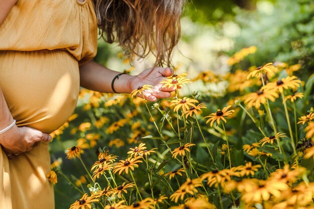 Seção média de mulher grávida tocando flores no parque