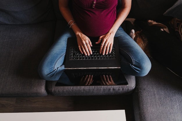 Seção média de mulher grávida usando laptop enquanto está sentada no sofá em casa