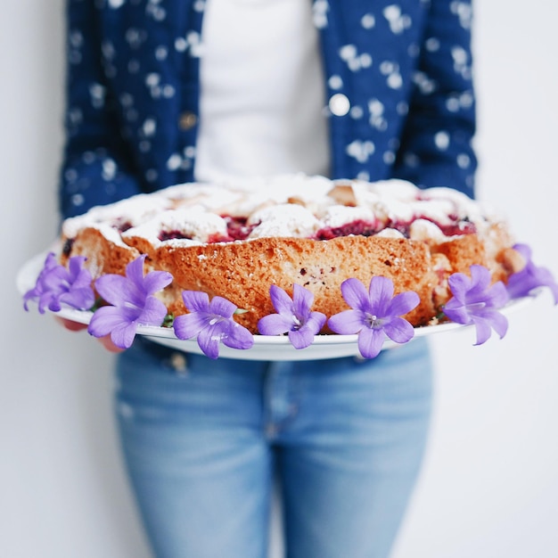 Foto seção média de mulher segurando bolo de cereja fresco com flores roxas