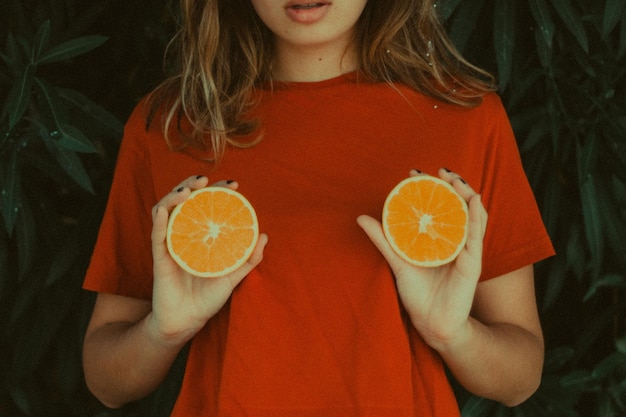 Seção média de mulher segurando fatias de laranja por plantas
