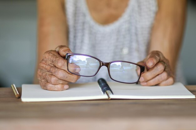 Foto seção média de mulher segurando óculos sobre um livro na mesa