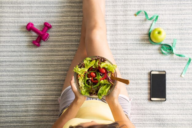 Seção média de mulher segurando salada em uma tigela enquanto está sentada na cama em casa