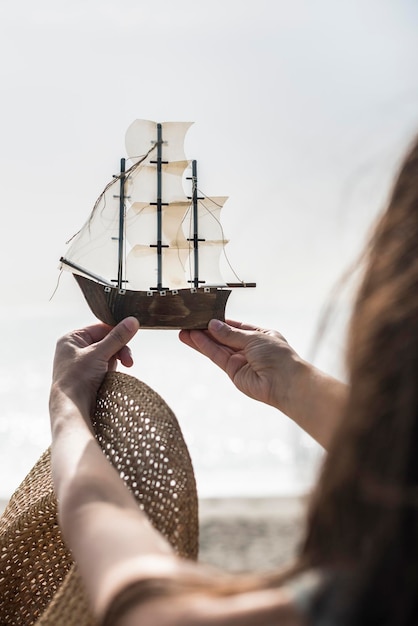 Foto seção média de mulher segurando um barco de brinquedo na praia contra o céu