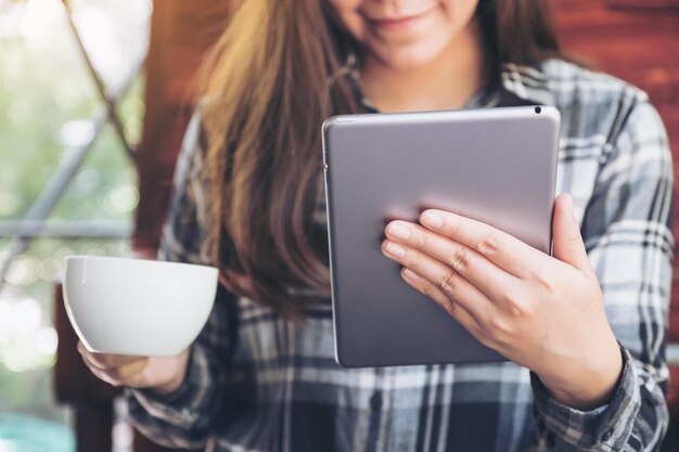 Foto seção média de mulher segurando xícara de café e tablet digital em um café