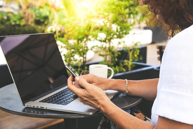 Foto seção média de mulher usando laptop e telefone móvel enquanto está sentada na mesa em um café