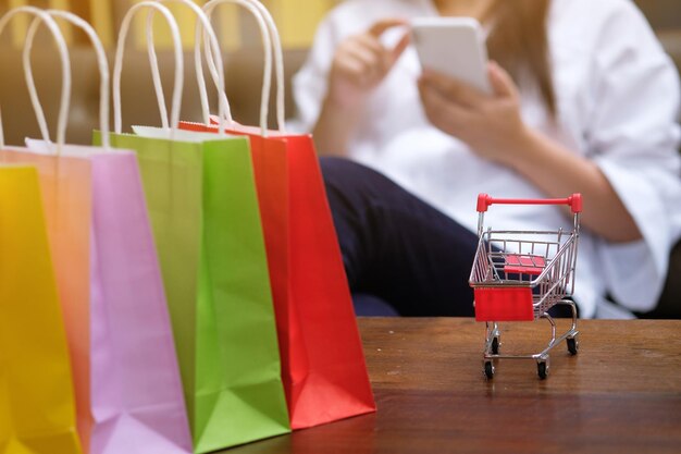 Foto seção média de mulher usando telefone celular com sacos de compras e carrinho de estatuetas na mesa