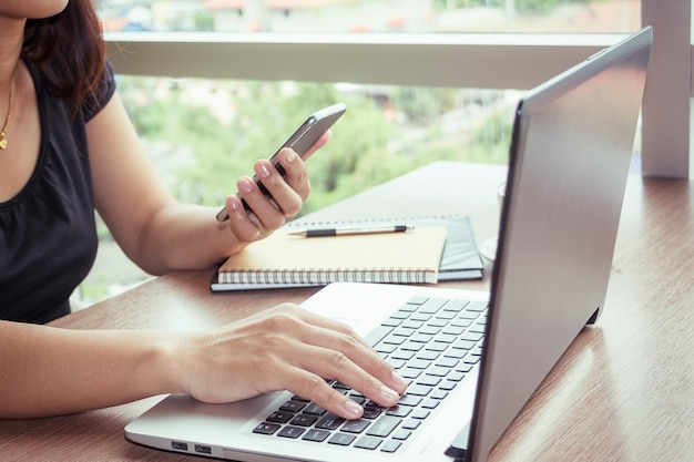 Seção média de mulher usando telefone celular e laptop na mesa
