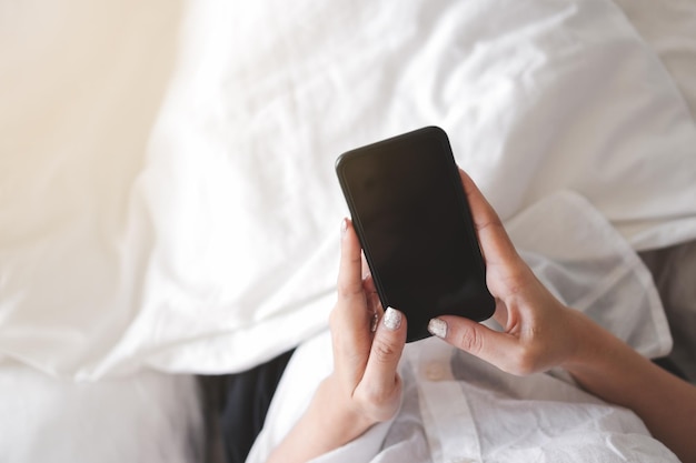 Seção média de mulher usando telefone móvel na cama