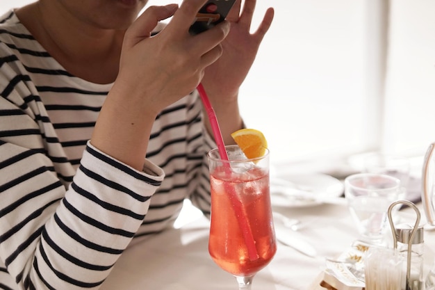 Seção média de mulher usando telefone móvel por bebida na mesa