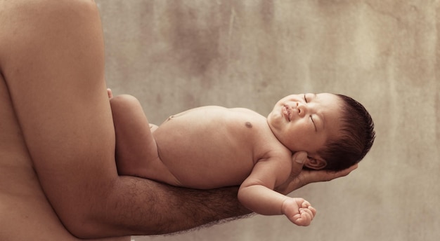 Foto seção média de pai sem camisa segurando filho recém-nascido contra a parede