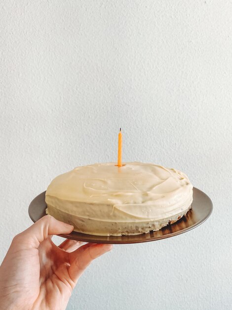 Foto seção média de pessoa segurando bolo de aniversário contra a parede branca