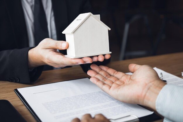 Seção média de um agente imobiliário dando uma casa modelo ao cliente na mesa