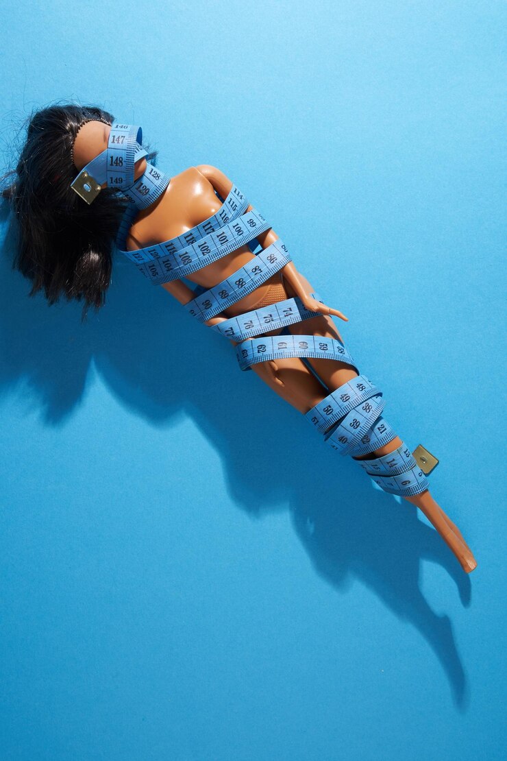 Foto seção média de um brinquedo de moda embrulhado com fita métrica de pé contra a parede azul
