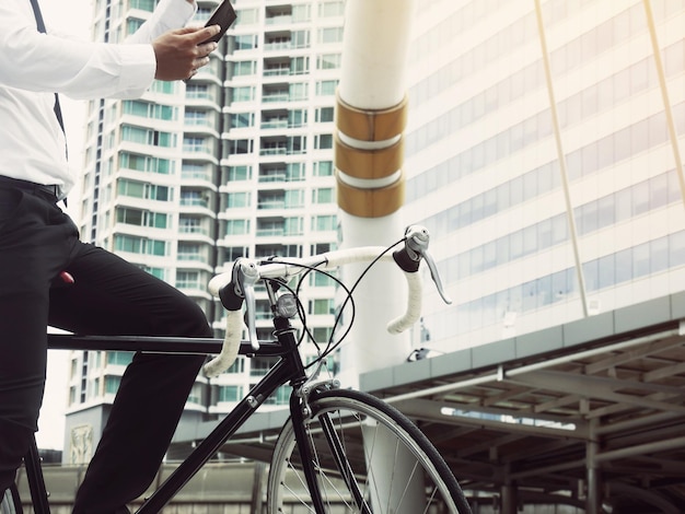 Foto seção média de um empresário com bicicleta usando um telefone inteligente contra um edifício na cidade