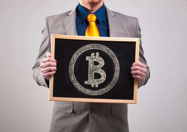 Foto seção média de um empresário segurando uma ardósia de escrita com sinal de bitcoin contra fundo branco