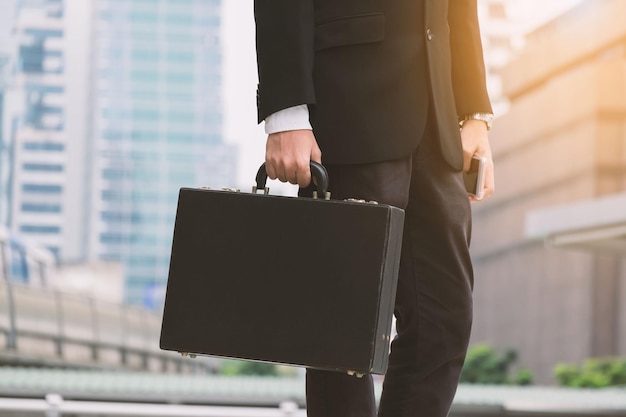 Seção média de um empresário segurando uma maleta enquanto está de pé contra edifícios