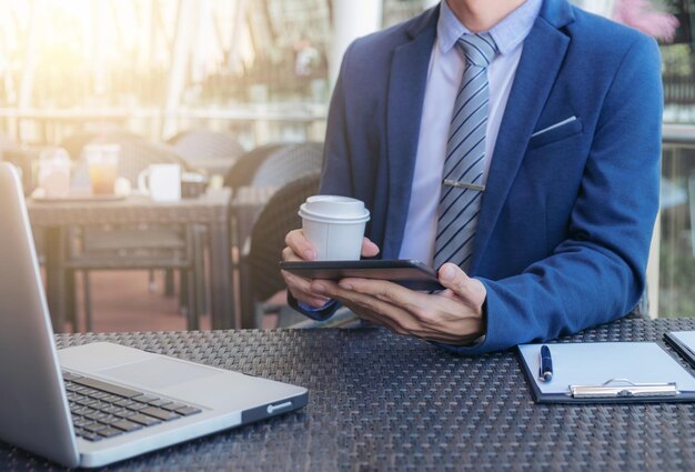 Foto seção média de um empresário segurando uma xícara de café enquanto usa tecnologia na mesa em um café