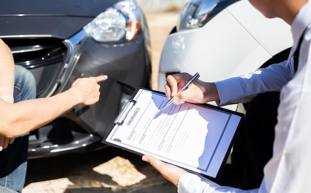 Foto seção média de um homem apontando para um carro enquanto um agente segurando uma caneta e um caderno agachado ao ar livre