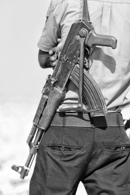 Foto seção média de um homem carregando uma arma enquanto está de pé ao ar livre