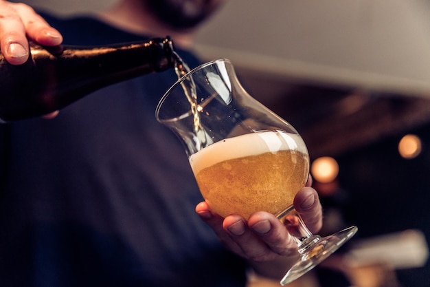 Seção média de um homem enchendo um copo de vinho com cerveja