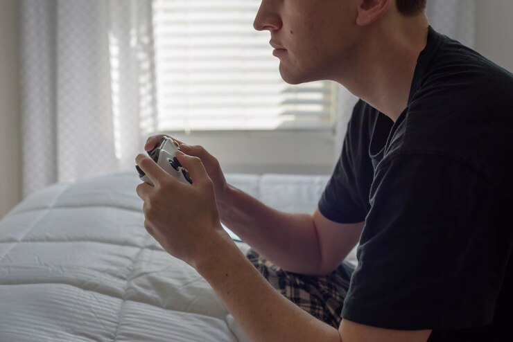 Foto seção média de um homem jogando videogame enquanto está sentado na cama