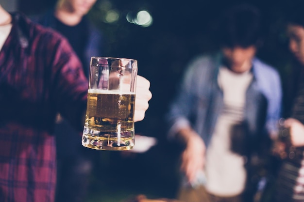 Foto seção média de um homem segurando cerveja enquanto está com amigos no quintal durante a noite