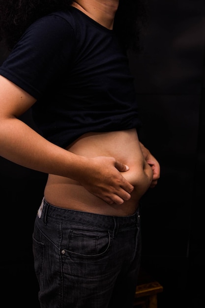 Foto seção média de um homem segurando o estômago enquanto está de pé contra um fundo preto