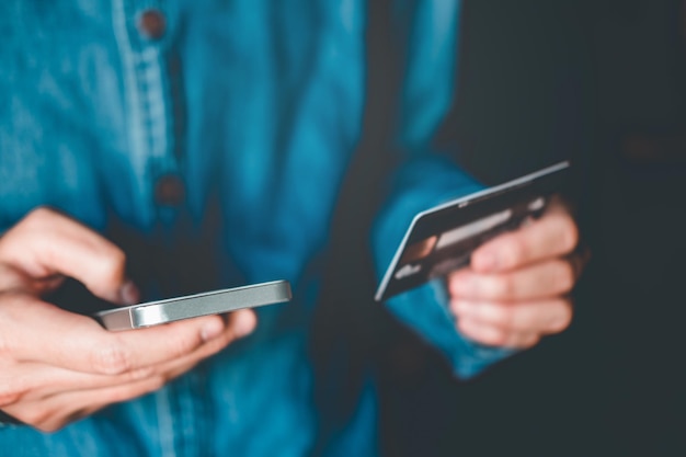 Seção média de um homem segurando um cartão de crédito enquanto usa um telefone celular