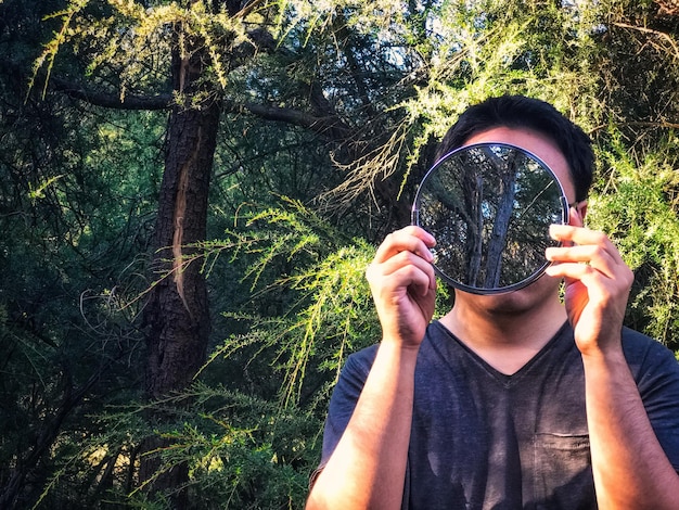 Foto seção média de um homem segurando um espelho na floresta