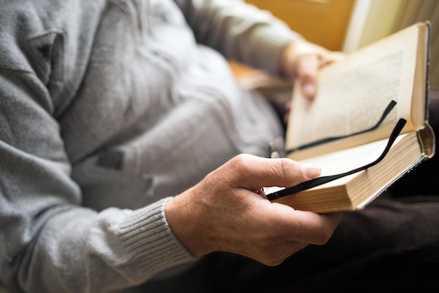 Seção média de um homem segurando um livro e óculos em casa