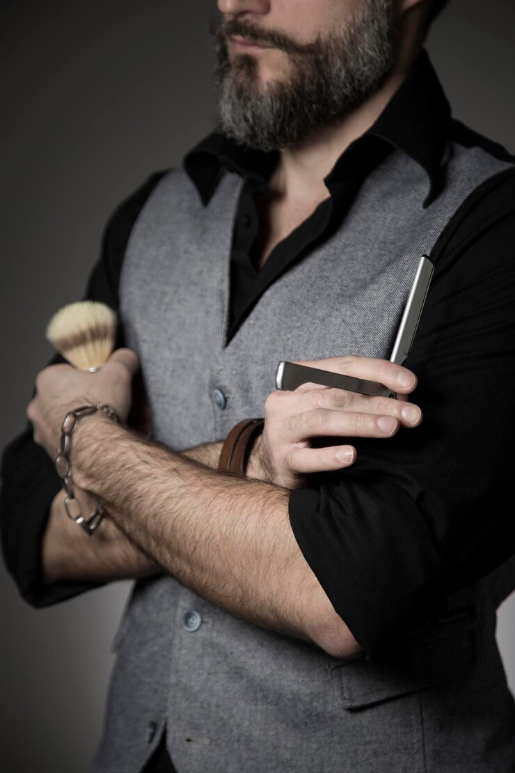 Foto seção média de um homem segurando uma escova de barbear e uma navalha contra um fundo cinzento