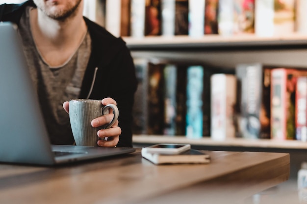 Seção média de um homem segurando uma xícara de café enquanto usa um laptop na mesa