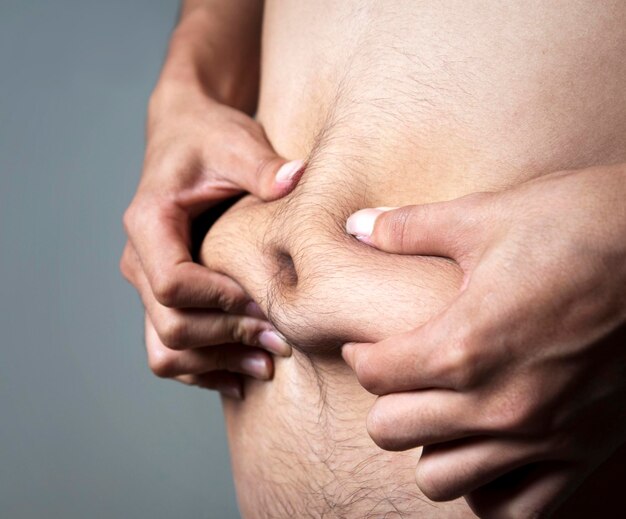 Foto seção média de um homem sem camisa segurando a barriga contra um fundo cinzento