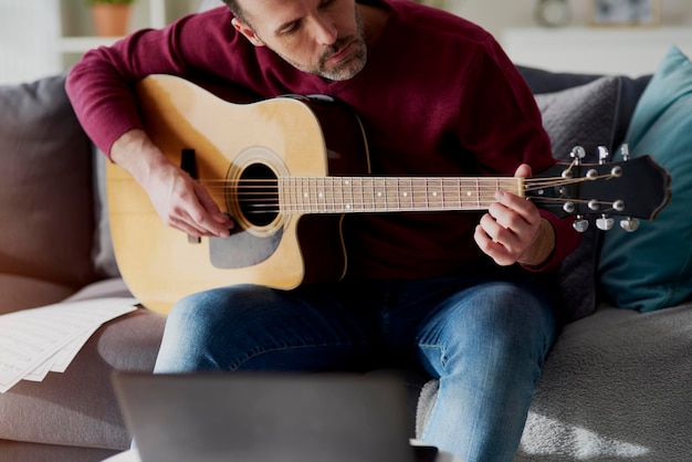 Seção média de um homem tocando guitarra no sofá em casa