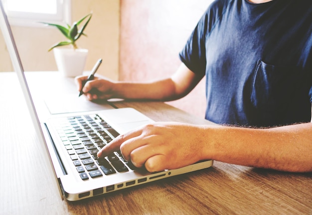 Seção média de um homem usando laptop em uma mesa de madeira