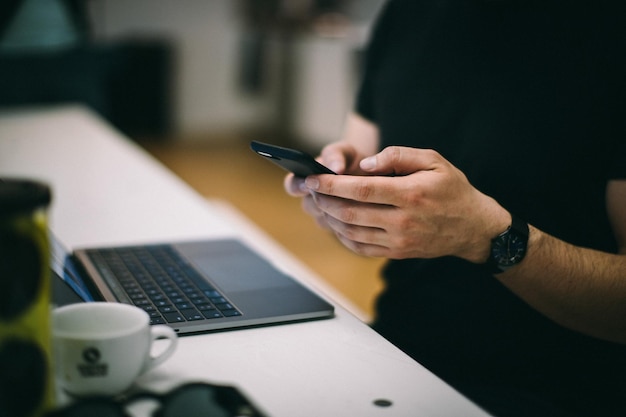 Seção média de um homem usando telefone móvel por laptop na mesa no escritório