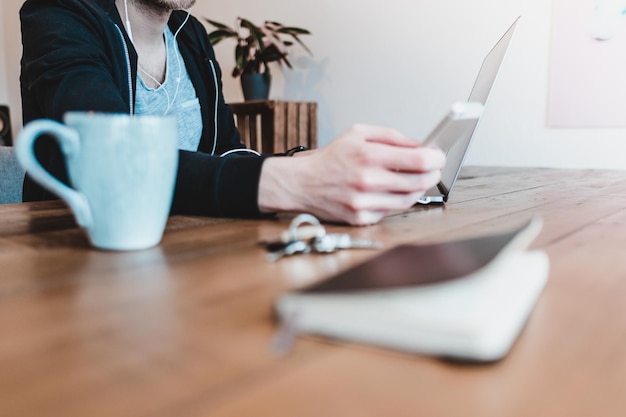 Seção média de um homem usando um telefone inteligente na mesa em casa