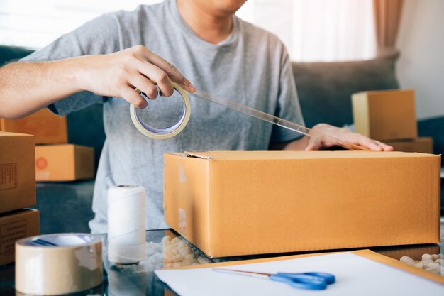 Foto seção média de um jovem embalando uma caixa de papelão na mesa em casa