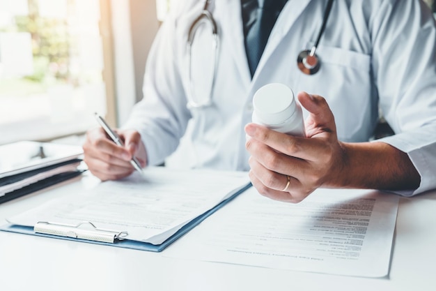 Seção média de um médico segurando uma garrafa enquanto escreve uma receita na mesa