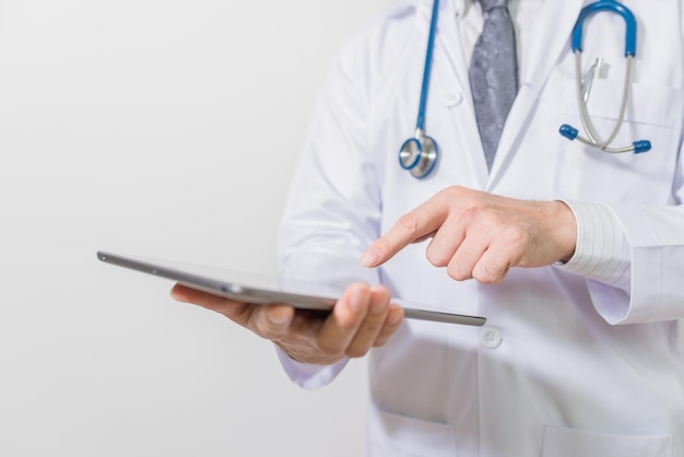 Seção média de um médico usando um tablet digital em pé contra um fundo branco