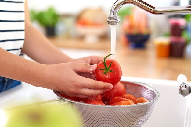 Seção média de uma adolescente lavando tomates na pia em casa