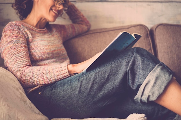 Seção média de uma jovem lendo um livro enquanto se relaxa no sofá em casa
