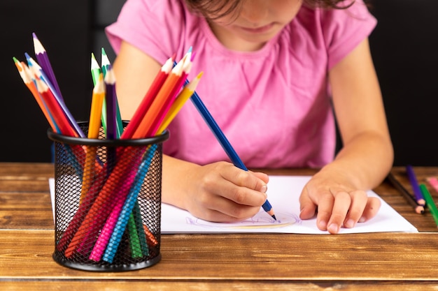 Seção média de uma menina desenhando em um livro na mesa