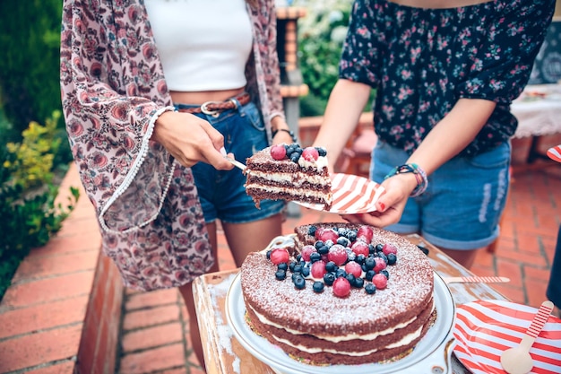 Seção média de uma mulher dando uma fatia de bolo para uma amiga no quintal