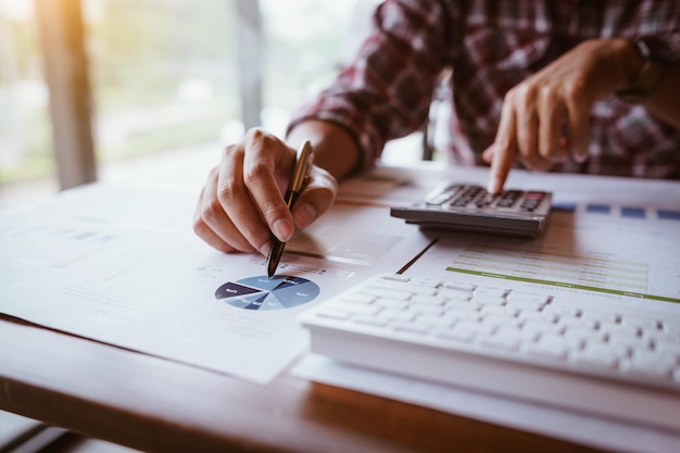 Seção média de uma mulher de negócios analisando gráficos enquanto usa uma calculadora na mesa