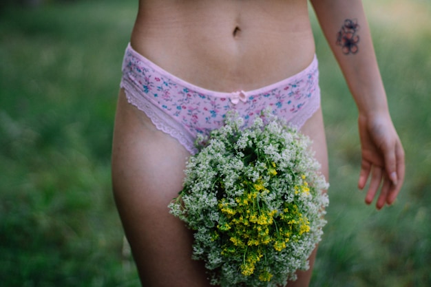 Seção média de uma mulher de pé junto a uma planta em flor